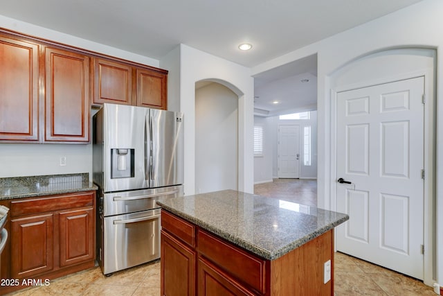 kitchen with dark stone countertops, a kitchen island, recessed lighting, arched walkways, and stainless steel refrigerator with ice dispenser