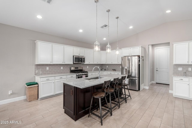 kitchen with lofted ceiling, sink, an island with sink, stainless steel appliances, and white cabinets