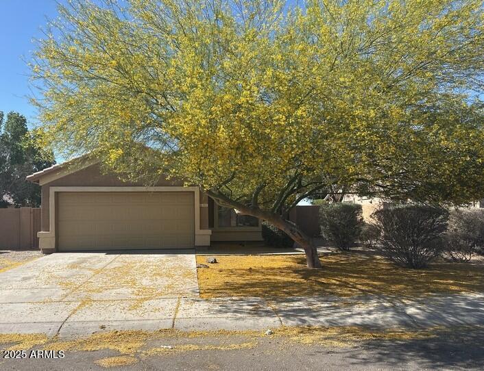 view of property hidden behind natural elements featuring stucco siding, driveway, and a garage