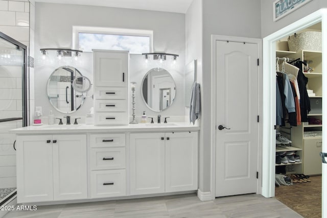 bathroom with a walk in closet, a shower stall, double vanity, and a sink