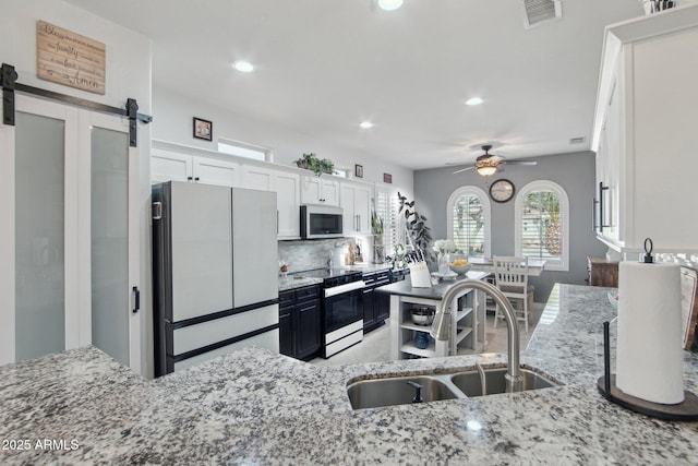 kitchen featuring visible vents, light stone counters, freestanding refrigerator, electric range, and a sink