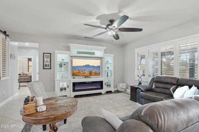 living area featuring a glass covered fireplace, light tile patterned flooring, baseboards, and ceiling fan