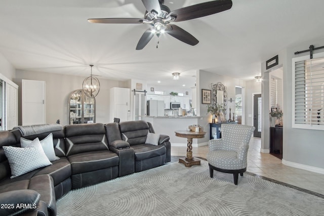 living area featuring ceiling fan with notable chandelier, a barn door, light tile patterned flooring, baseboards, and a healthy amount of sunlight