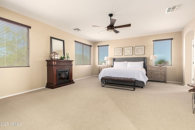 carpeted bedroom with a glass covered fireplace, visible vents, ceiling fan, and baseboards