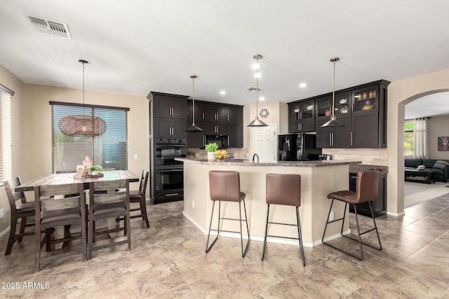 kitchen featuring decorative backsplash, black appliances, a breakfast bar area, visible vents, and arched walkways