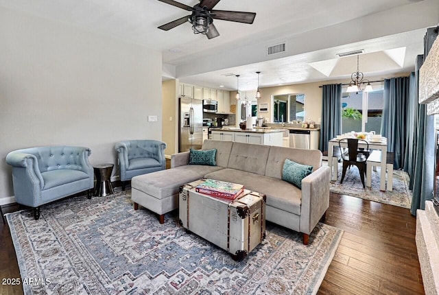 living area featuring dark wood finished floors, visible vents, and ceiling fan with notable chandelier