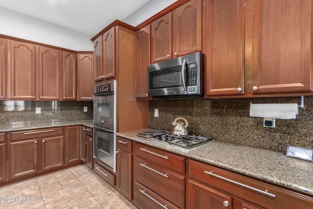 kitchen featuring appliances with stainless steel finishes, light tile patterned floors, light stone counters, and backsplash