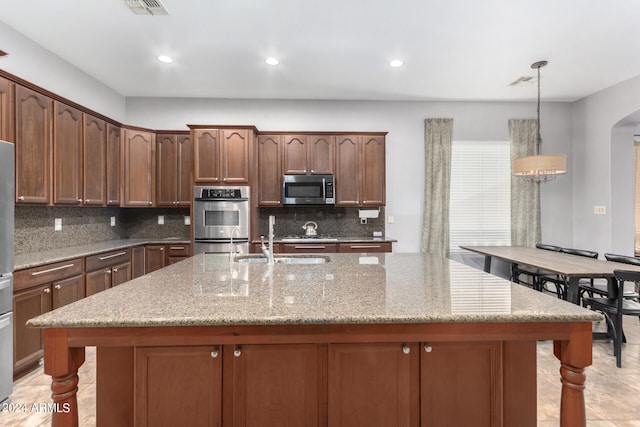 kitchen featuring decorative backsplash, stainless steel appliances, a center island with sink, and decorative light fixtures