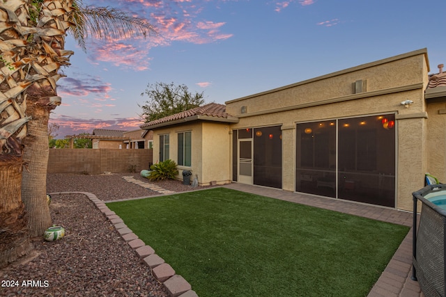 back house at dusk with a sunroom and a yard