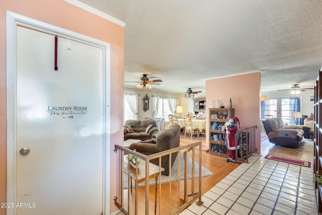 living room featuring ornamental molding, light tile patterned flooring, ceiling fan, and a textured ceiling