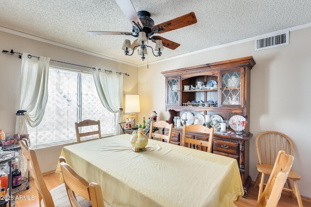 dining space with light wood-style flooring, visible vents, ceiling fan, and crown molding