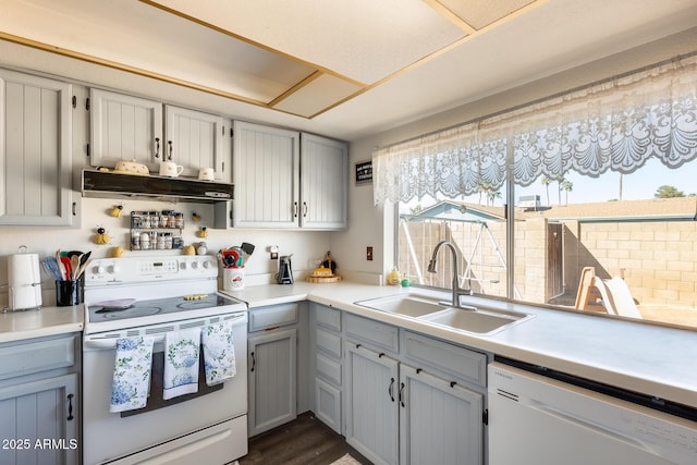 kitchen featuring light countertops, gray cabinetry, a sink, white appliances, and under cabinet range hood