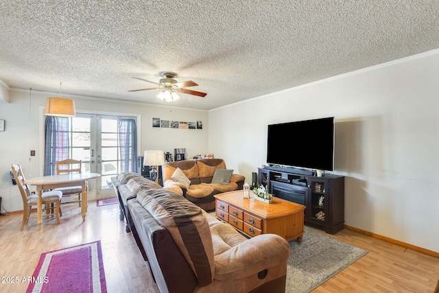 living area featuring ceiling fan, light wood-style flooring, baseboards, ornamental molding, and french doors