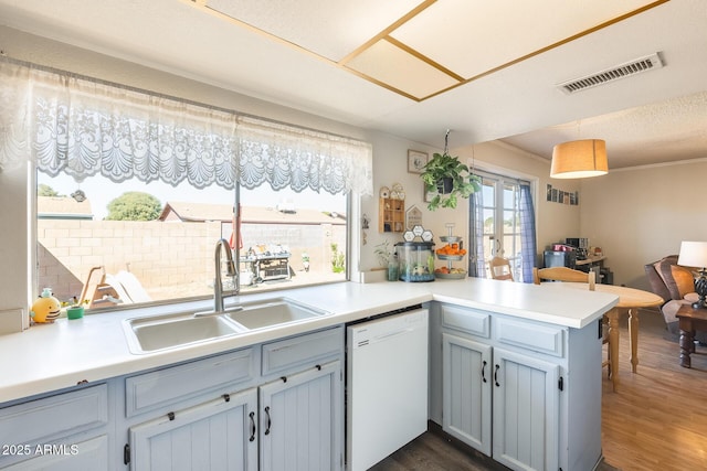 kitchen featuring dark wood-style floors, visible vents, a sink, dishwasher, and a peninsula