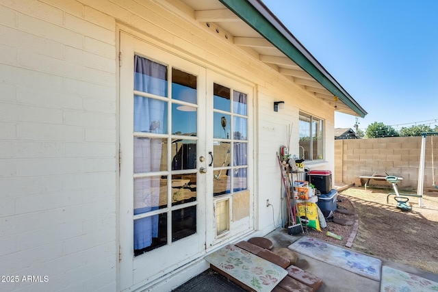 view of exterior entry with french doors, fence, and concrete block siding