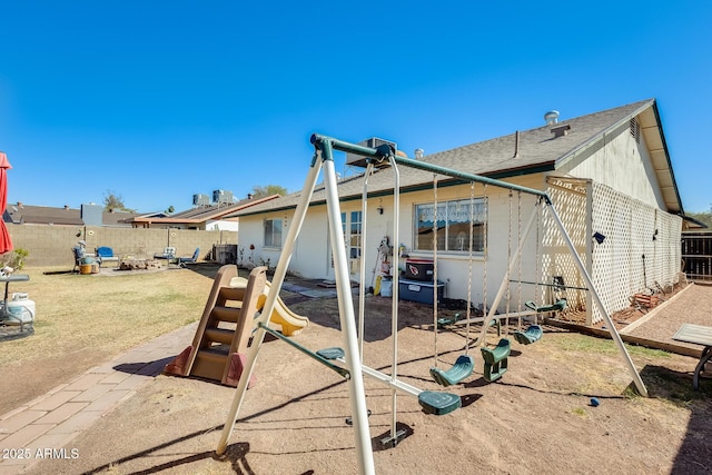 back of house featuring an outdoor fire pit, a shingled roof, a patio, a fenced backyard, and a playground