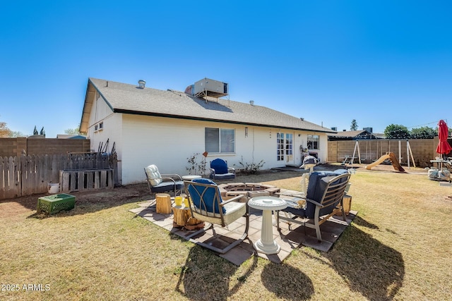 rear view of house with a fire pit, a playground, a lawn, and a fenced backyard