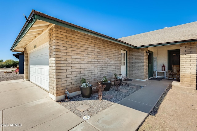 exterior space with a garage, concrete driveway, brick siding, and roof with shingles