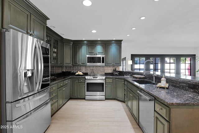 kitchen with backsplash, dark stone countertops, sink, light wood-type flooring, and stainless steel appliances