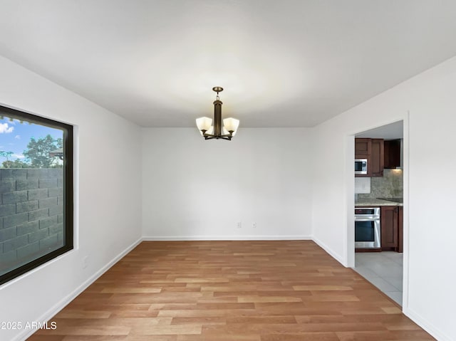 unfurnished dining area with a chandelier, light wood-type flooring, and baseboards