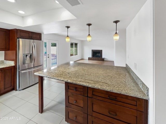 kitchen with visible vents, a peninsula, a brick fireplace, decorative light fixtures, and stainless steel fridge