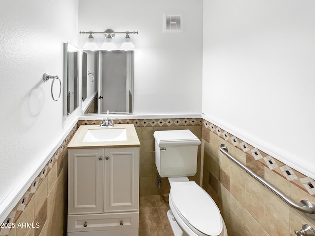 bathroom with visible vents, tile walls, a wainscoted wall, toilet, and vanity