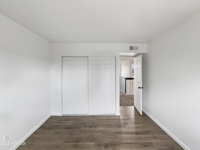 unfurnished bedroom featuring visible vents, baseboards, a closet, and wood finished floors