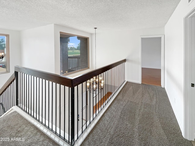 corridor featuring baseboards, a textured ceiling, an inviting chandelier, and carpet flooring