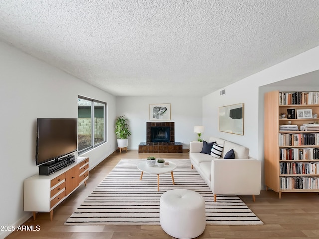 living room with visible vents, a tile fireplace, a textured ceiling, and wood finished floors