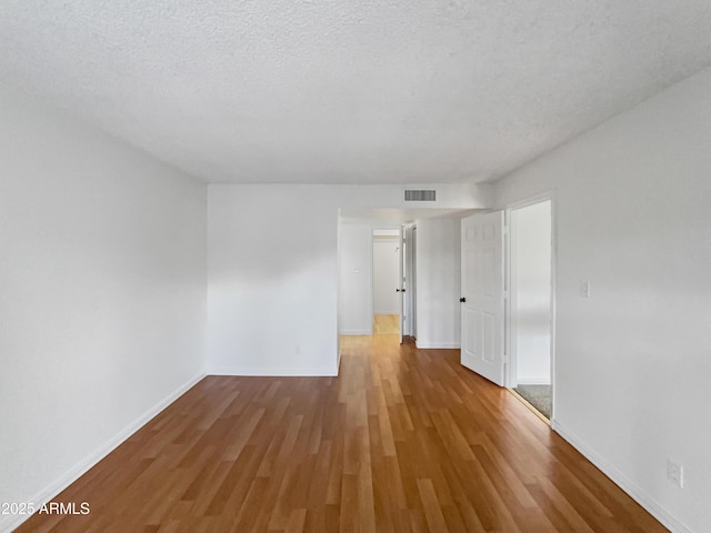 spare room with visible vents, a textured ceiling, baseboards, and wood finished floors