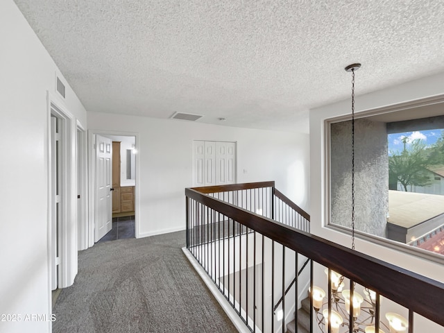 hall with visible vents, baseboards, an upstairs landing, a textured ceiling, and dark colored carpet