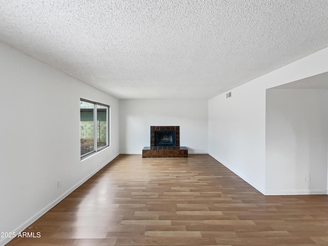 unfurnished living room featuring visible vents, a fireplace, baseboards, and wood finished floors