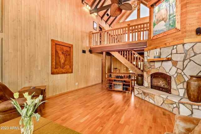 living room with high vaulted ceiling, ceiling fan, hardwood / wood-style flooring, wooden walls, and a fireplace