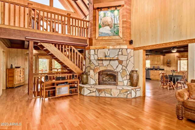 living room featuring high vaulted ceiling, a stone fireplace, ceiling fan, wood-type flooring, and wooden walls