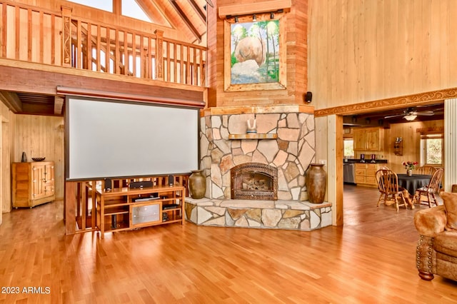 living room with high vaulted ceiling, wood walls, ceiling fan, wood-type flooring, and a fireplace