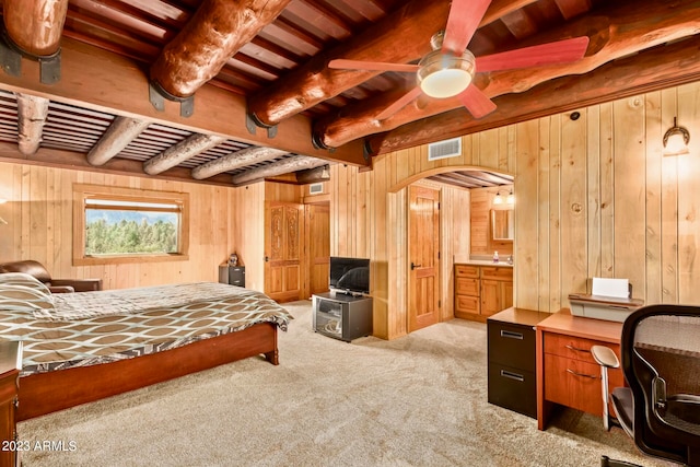 bedroom with light colored carpet, wood walls, ceiling fan, and beam ceiling