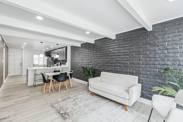 living room featuring sink, beam ceiling, light hardwood / wood-style floors, and brick wall