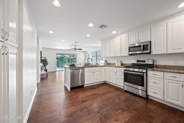 kitchen with sink, kitchen peninsula, dark stone counters, white cabinets, and appliances with stainless steel finishes