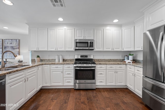 kitchen featuring appliances with stainless steel finishes, light stone counters, dark wood-type flooring, sink, and white cabinetry