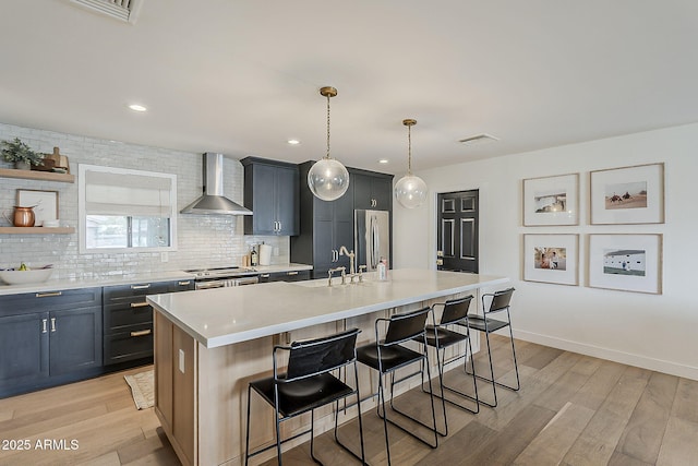 8320 E Monte Vista Rd, Scottsdale, AZ 85257 - kitchen with wall chimney exhaust hood, appliances with stainless steel finishes, light wood-style floors, a kitchen bar, and light countertops
