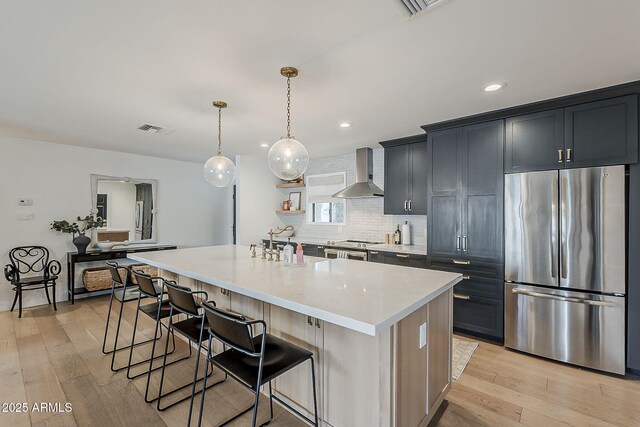 8320 E Monte Vista Rd, Scottsdale, AZ 85257 - kitchen with stainless steel appliances, wall chimney range hood, backsplash, a kitchen breakfast bar, and light wood finished floors