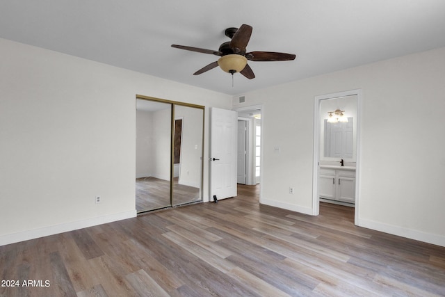 unfurnished bedroom featuring ceiling fan, ensuite bathroom, light hardwood / wood-style floors, and a closet