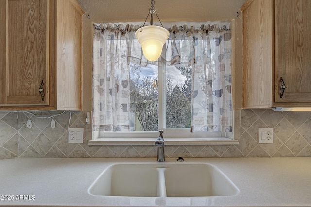 kitchen featuring decorative backsplash, light brown cabinetry, hanging light fixtures, and sink