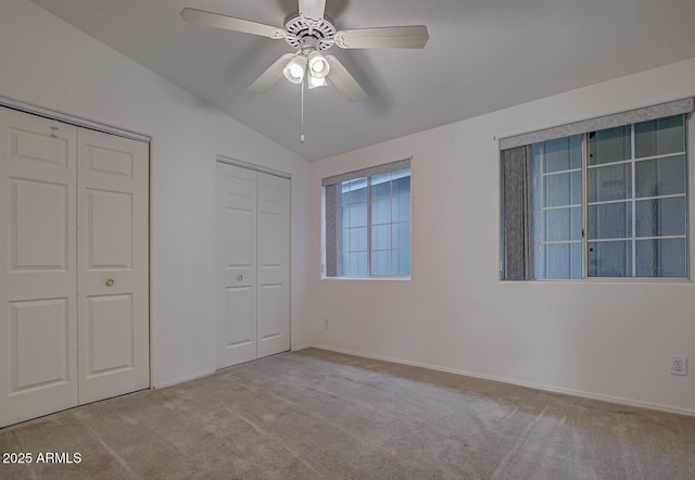 unfurnished bedroom with ceiling fan, light colored carpet, lofted ceiling, and multiple closets