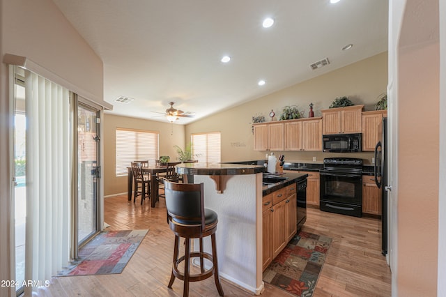 kitchen with black appliances, a center island, vaulted ceiling, a breakfast bar, and light wood-type flooring