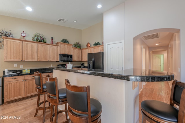 kitchen with a kitchen island, a kitchen breakfast bar, light brown cabinetry, light wood-type flooring, and black appliances