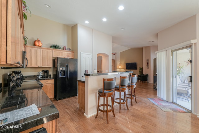 kitchen with vaulted ceiling, black appliances, a center island, and light wood-type flooring