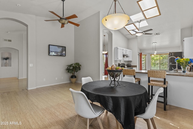 1135 W Sea Fog Dr, Gilbert, AZ 85233 - dining room with a ceiling fan, arched walkways, a skylight, high vaulted ceiling, and light wood-type flooring