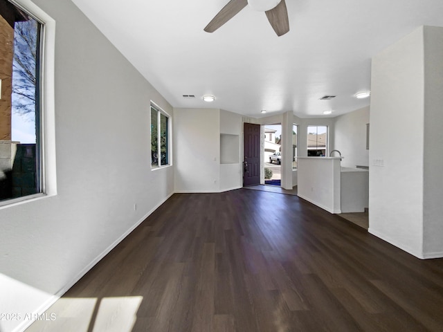 unfurnished living room with ceiling fan, visible vents, baseboards, and dark wood-style flooring