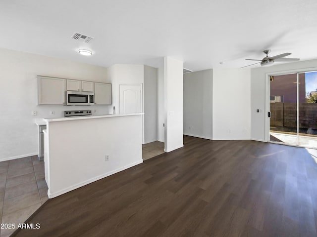 kitchen featuring ceiling fan, stainless steel appliances, light countertops, gray cabinets, and dark wood finished floors